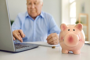 elderly man looking into his investments with a piggy bank on his desk